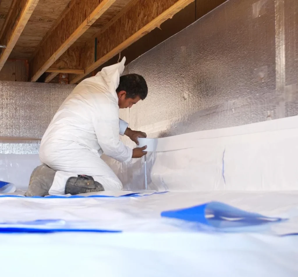 Technician sealing a crawl space wall vapor barrier in Fort Mill, NC